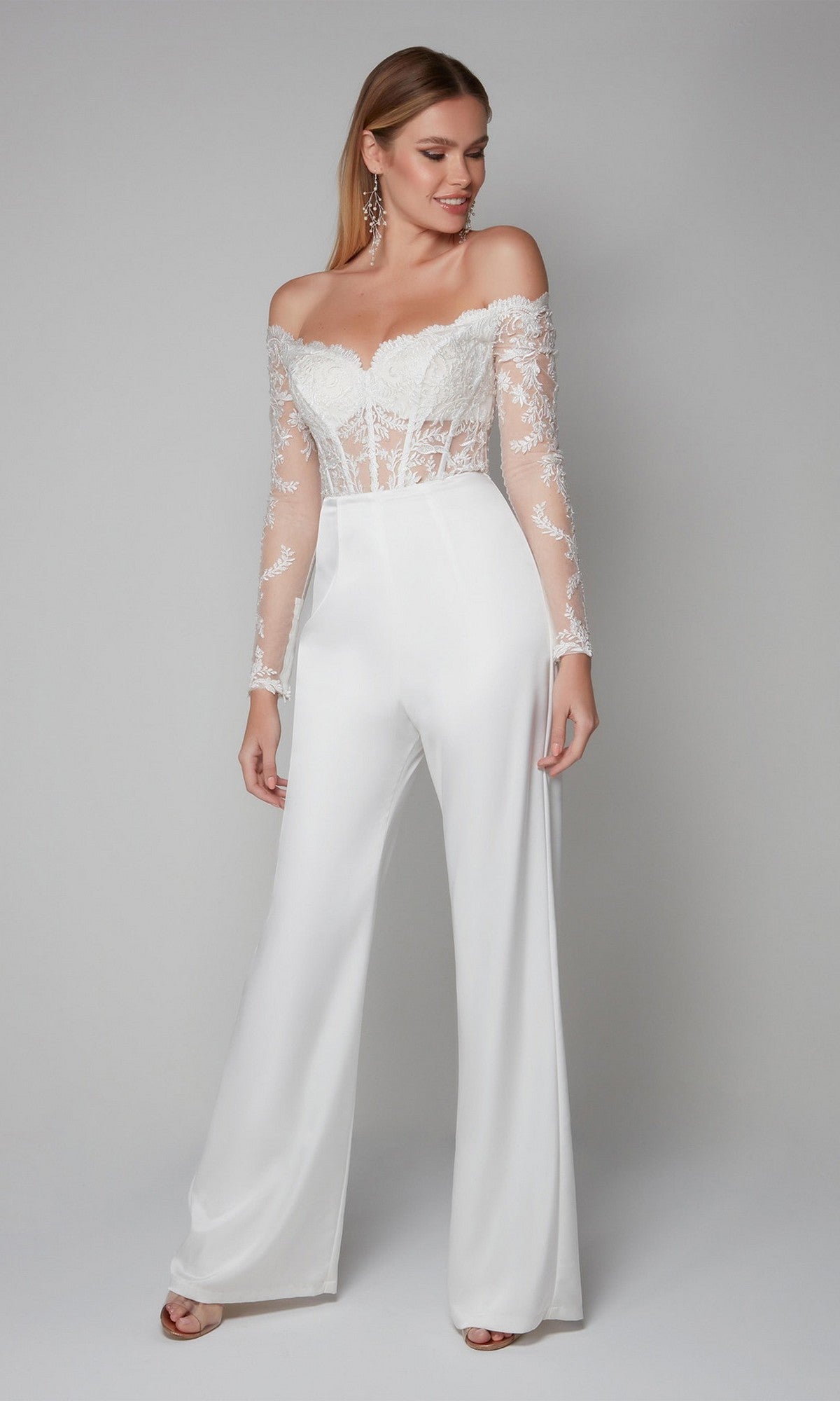 Woman wearing the Alyce 70018 Long Formal Jumpsuit in Diamond White, featuring off-the-shoulder lace with sheer sleeves and wide-leg pants, stands against a light gray background.
